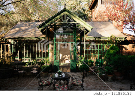 A charming green house featuring a table and chairs situated in front of it A charming green house featuring a table and chairs situated in front of it 121886153
