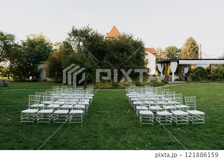 A row of pristine white chairs is neatly lined up in a grassy field 121886159