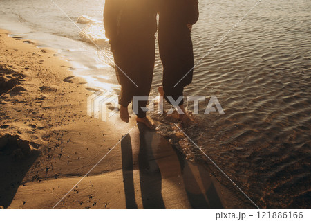 A couple is leisurely walking barefoot along the beach by the waters edge 121886166
