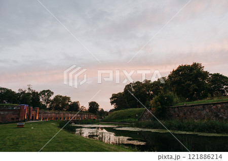 A river with trees and grass, set against a sunset backdrop 121886214