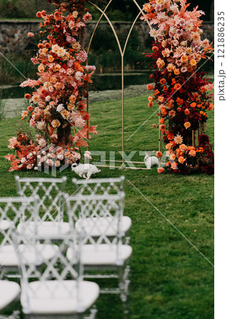 A row of white chairs is lined up before a beautiful floral arch 121886235