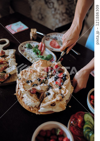 A person is cutting a cake topped with strawberries and blueberries 121886309