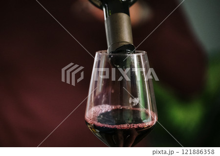 A bottle containing red wine is currently being poured into a glass A bottle containing red wine is currently being poured into a glass 121886358