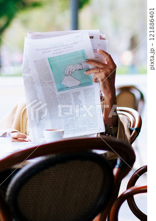 An individual is sitting comfortably at a table engaged in reading a newspaper 121886401