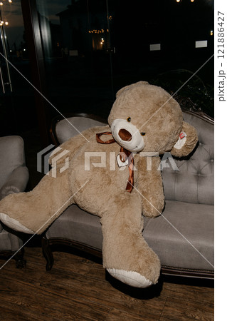A large, fluffy teddy bear is comfortably sitting on a cozy couch A large, fluffy teddy bear is comfortably sitting on a cozy couch 121886427