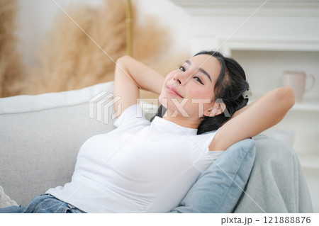 Copy space shot of young woman reclining on sofa with hands behind head and relaxing happily 121888876