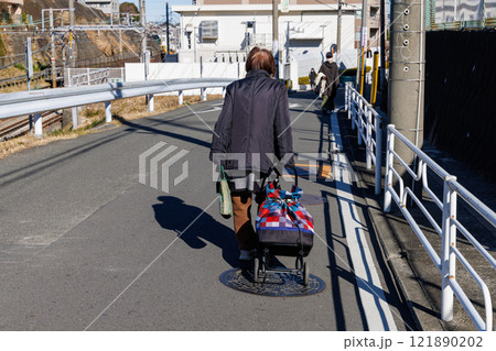 買い物カゴを引いて歩く老人の後ろ姿 121890202