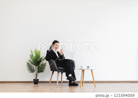 Young Asian woman in business attire participates in online video call, sitting in modern office setting, with friendly demeanor. Young Asian woman in business attire participates in online video call, sitting in modern office setting, with friendly demeanor. 121894089