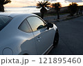 夕焼けの海沿いに止まる、白いスポーツカー 121895460