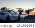 夕焼けの海沿いに止まる、白いスポーツカー 121895461