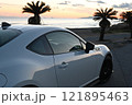 夕焼けの海沿いに止まる、白いスポーツカー 121895463