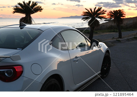 夕焼けの海沿いに止まる、白いスポーツカー 夕焼けの海沿いに止まる、白いスポーツカー 121895464