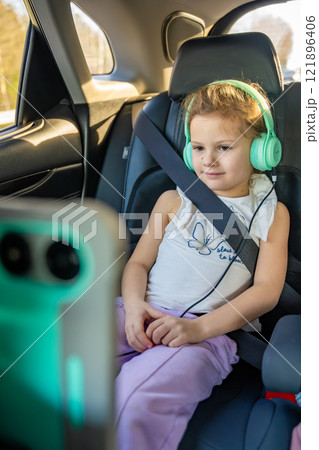 Little girl with tablet and headphones in the car during travel on vacation. Entertainment in the transport for child Little girl with tablet and headphones in the car during travel on vacation. Entertainment in the transport for child 121896406