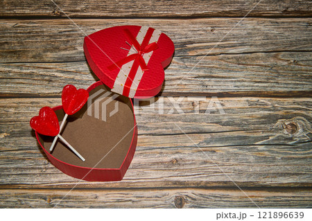 Two lollipops in a red heart box on a wooden table 121896639