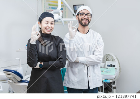 Portrait of dentist and her assistant in the office, female dentist and her assistant thumbs up, oral professionals portrait 121897741