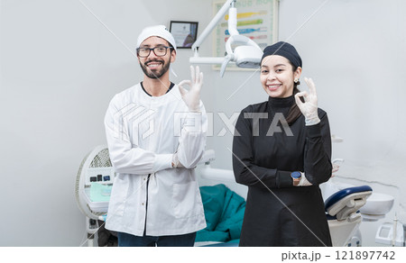 Portrait of dentist and her assistant in the office, female dentist and her assistant thumbs up, oral professionals portrait 121897742