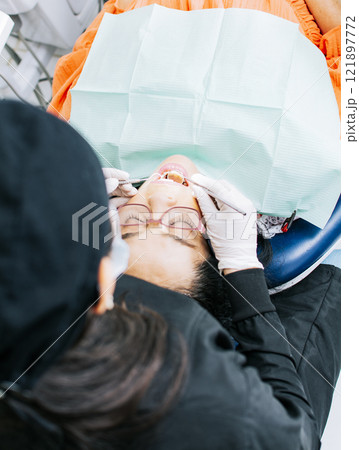 View back of dentist with patient ; Woman dentist doing endodontics to woman patient; Dentist examining mouth to patient; Dentist performing stomatology 121897772