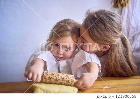 a family with two daughters, a teenager and a toddler, cook cookies together in the kitchen, sisterly love 121900359