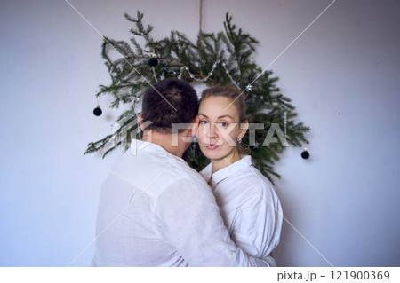 a middle-aged couple in love hug in front of a wreath of needles, a Christmas tree a middle-aged couple in love hug in front of a wreath of needles, a Christmas tree 121900369