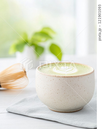 creamy matcha latte in ceramic cup with latte art, placed on light cloth 121901093