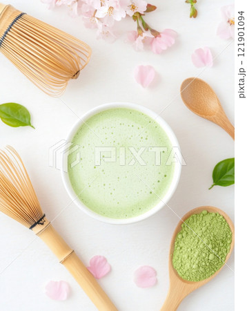 Matcha tea with frothy texture surrounded by bamboo whisks, powder, and cherry blossoms 121901094