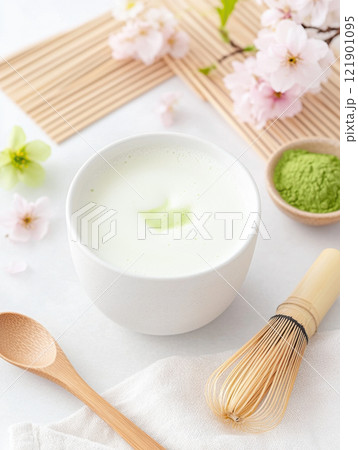 Creamy matcha latte with cherry blossoms and bamboo whisk on white background 121901095
