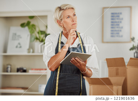 Tailor, textile and mature fashion designer thinking and planning or browsing on a tablet in a trendy and stylish small business. Checking an online clothing order on her company website 121901636