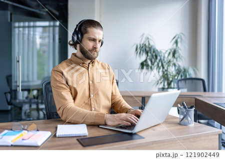 Focused business professional wearing headphones and working diligently on a laptop in an office. The image portrays concentration, productivity, and a professional work environment Focused business professional wearing headphones and working diligently on a laptop in an office. The image portrays concentration, productivity, and a professional work environment 121902449