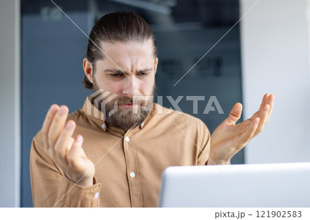 A man looks perplexed as he gestures toward his laptop, reflecting confusion at work. A man looks perplexed as he gestures toward his laptop, reflecting confusion at work. 121902583
