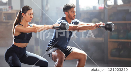 Slim, fit and gym couple exercising with dumbbell equipment, doing lower body core workout or training in a wellness facility. Young woman and man doing squatting exercise for perfect form or health Slim, fit and gym couple exercising with dumbbell equipment, doing lower body core workout or training in a wellness facility. Young woman and man doing squatting exercise for perfect form or health 121903230