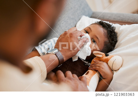 Sick, ill and unwell little boy suffering from cold, flu or covid and lying on the sofa at home while blowing his nose with dad. Cute son with a runny nose and resting in the living room from above 121903363