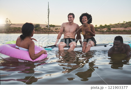 Laughing friends, swimming and playful bonding on summer break with pool inflatable tube in lake, ocean or sea. Diverse group of men or women having fun together and being social on holiday at sunset Laughing friends, swimming and playful bonding on summer break with pool inflatable tube in lake, ocean or sea. Diverse group of men or women having fun together and being social on holiday at sunset 121903377