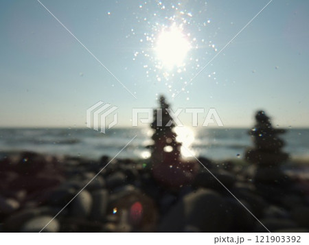 defocused background with stone paramids on the seashore and the sun in the blue sky, blur copy space on the theme of relaxation and tranquility on the ocean shore with a pyramid of stones defocused background with stone paramids on the seashore and the sun in the blue sky, blur copy space on the theme of relaxation and tranquility on the ocean shore with a pyramid of stones 121903392