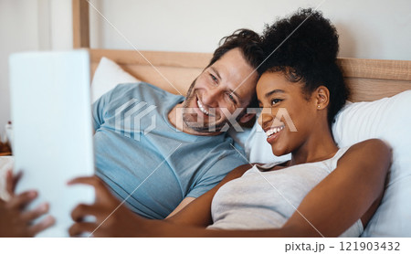 Happy, relax and carefree interracial couple on digital tablet smiling and taking a selfie in bed. Husband and wife waking up and reading social media news on touchscreen while relaxing at home. Happy, relax and carefree interracial couple on digital tablet smiling and taking a selfie in bed. Husband and wife waking up and reading social media news on touchscreen while relaxing at home. 121903432