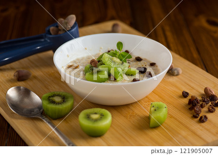 cooked oatmeal with kiwi, honey and nuts in a bowl on a wooden table cooked oatmeal with kiwi, honey and nuts in a bowl on a wooden table 121905007