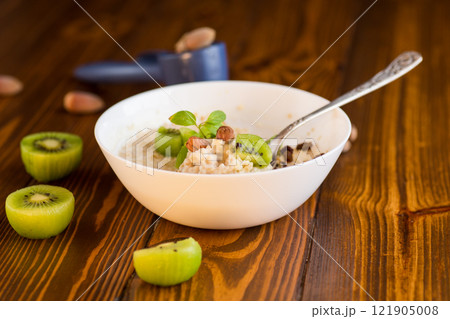 cooked oatmeal with kiwi, honey and nuts in a bowl on a wooden table cooked oatmeal with kiwi, honey and nuts in a bowl on a wooden table 121905008