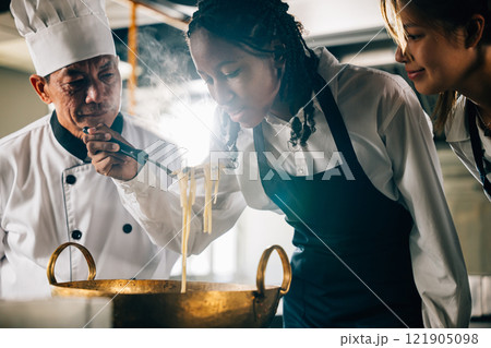 In kitchen chef teaches noodle cooking to students. Schoolgirls in uniform make ramen soup. Teacher guides kids at stove. Modern education in action joyful learning. Foor Education Concept In kitchen chef teaches noodle cooking to students. Schoolgirls in uniform make ramen soup. Teacher guides kids at stove. Modern education in action joyful learning. Foor Education Concept 121905098