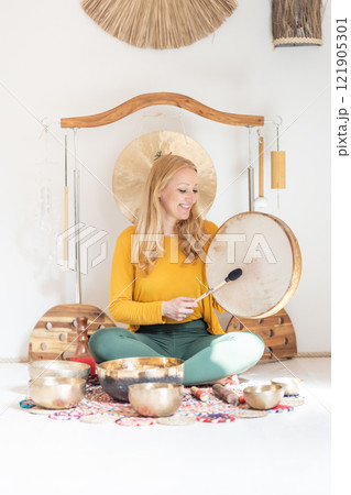 Young cheerful woman performing music therapy session with traditional instruments. Sound meditation, body healing. Seven chakras. Healthcare recreation process Young cheerful woman performing music therapy session with traditional instruments. Sound meditation, body healing. Seven chakras. Healthcare recreation process 121905301