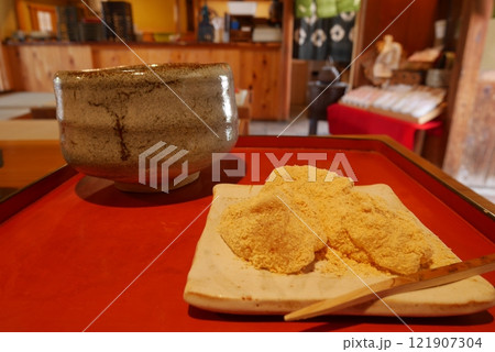 風情のある和風の茶屋で赤い盆に乗せられたきなこをまぶした葛餅と抹茶の入った茶器 121907304