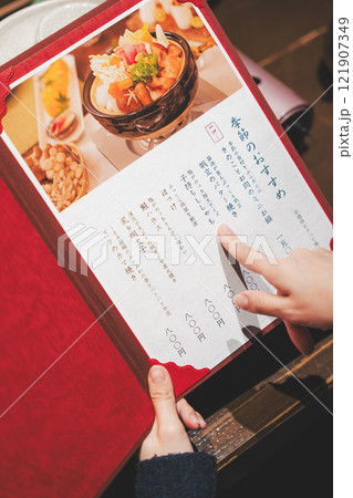 メニューを見て選ぶ女性客の手【撮影協力・海鮮居酒屋 魚魯こ】 メニューを見て選ぶ女性客の手【撮影協力・海鮮居酒屋 魚魯こ】 121907349