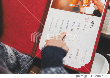 メニューを見て選ぶ女性客の手【撮影協力・海鮮居酒屋 魚魯こ】 メニューを見て選ぶ女性客の手【撮影協力・海鮮居酒屋 魚魯こ】 121907420