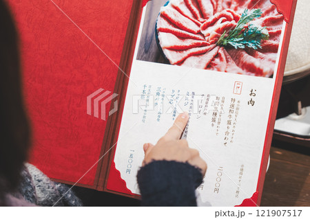 メニューを見て選ぶ女性客の手【撮影協力・海鮮居酒屋　魚魯こ】 121907517