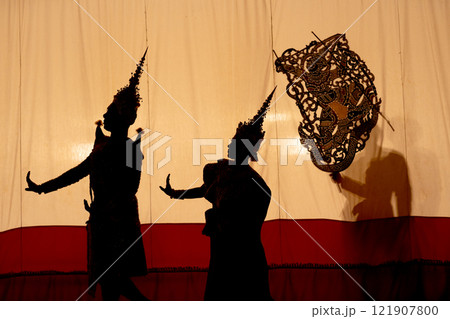 Silhouette and wide shot of man and woman with Khon or Mask dance costume stand with performance action in front of grand shadow play in the background with white screen. Silhouette and wide shot of man and woman with Khon or Mask dance costume stand with performance action in front of grand shadow play in the background with white screen. 121907800
