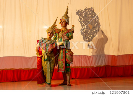 Wide shot of man and woman with Khon or Mask dance costume stand with performance action in front of grand shadow play in the background with white screen. 121907801