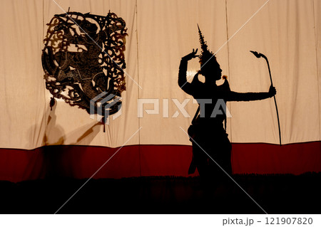 Silhouette of Khon or Mask dance player stand with performance action in front of grand shadow play in the background with white screen. Silhouette of Khon or Mask dance player stand with performance action in front of grand shadow play in the background with white screen. 121907820