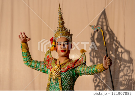 Man with Khon or Mask dance costume stand with performance action in front of grand shadow play in the background with white screen. Man with Khon or Mask dance costume stand with performance action in front of grand shadow play in the background with white screen. 121907885