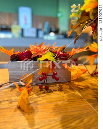 Autumn centerpiece with artificial leaves, berries, and pinecones in a wooden box on a rustic wooden table. Warm tones of orange, red, and yellow evoke a cozy seasonal atmosphere, perfect for autumn 121907932