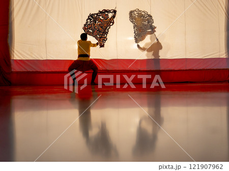 The player men stand with perform grand shadow play with one stand in front of white screen with reflection on the floor. 121907962