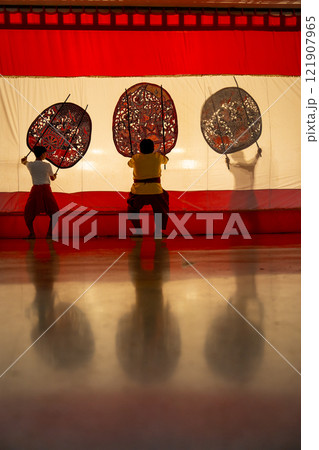 Vertical image of three player men stand with perform grand shadow play with two stay in front of white screen with reflection on the floor. Vertical image of three player men stand with perform grand shadow play with two stay in front of white screen with reflection on the floor. 121907965
