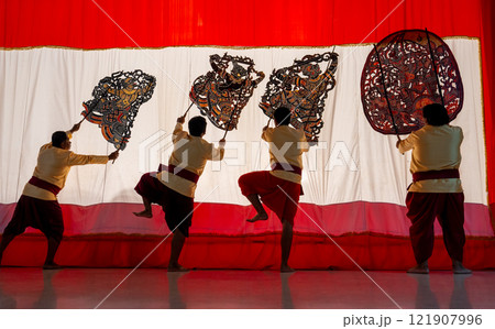 Four player men stand with perform grand shadow play in front of white screen with some of them lift leg as performance of the show. 121907996
